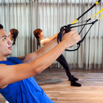 Two people exercising using a TRX and their body weight for resistance.